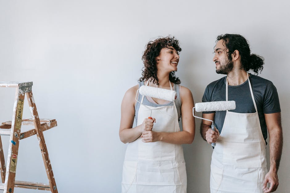 A Couple Standing By The Wall Holding Paint Rollers