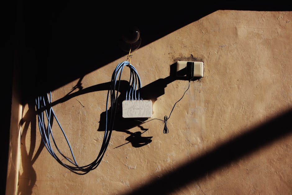 Electric blue wires connected to network adapter plugged in socket on shabby brown wall of building on street with shadow