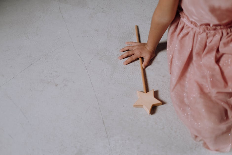 A Girl in a Pink Dress Sitting on the Floor Holding a Wand