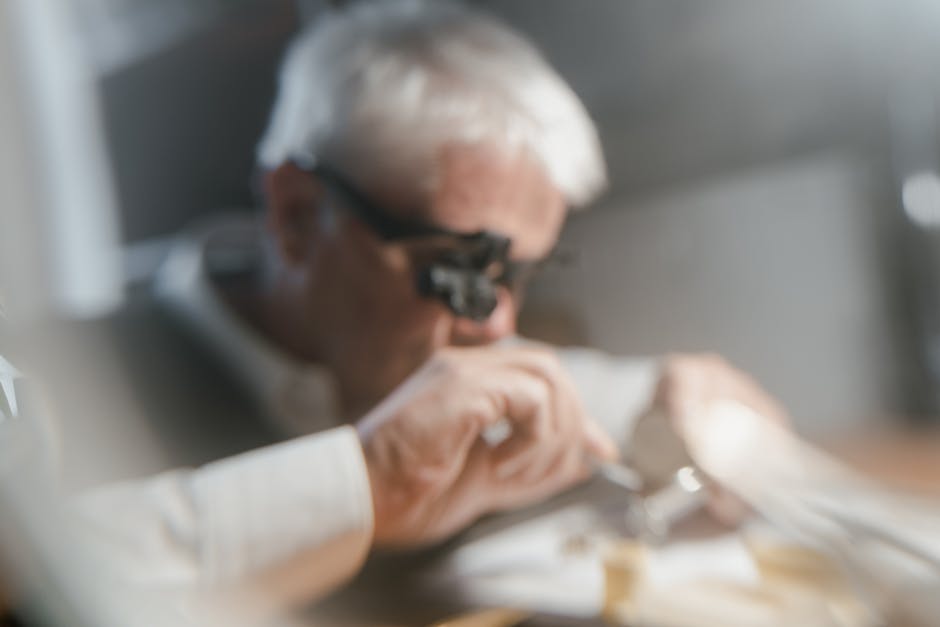 Blurry Photo of an Elderly Man Wearing a Magnifying Glass and Fixing an Item