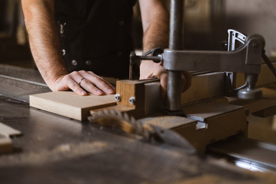 Unrecognizable male master cutting piece of wooden plank while working at sawbench in workshop on blurred background with professional equipment