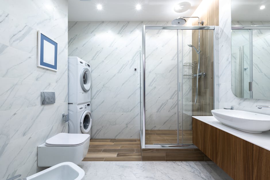 Contemporary bathroom toilet near tiled wall against cabinet with sink placed near shower cabin with glass wall and washing machines