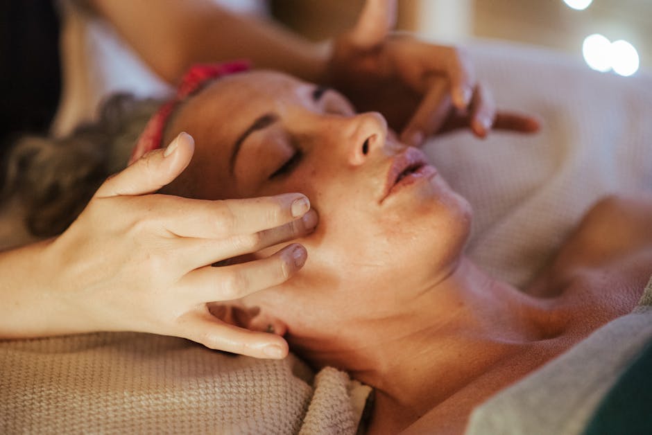 Adult woman relaxing in spa salon on comfortable bed while getting face massage from masseur