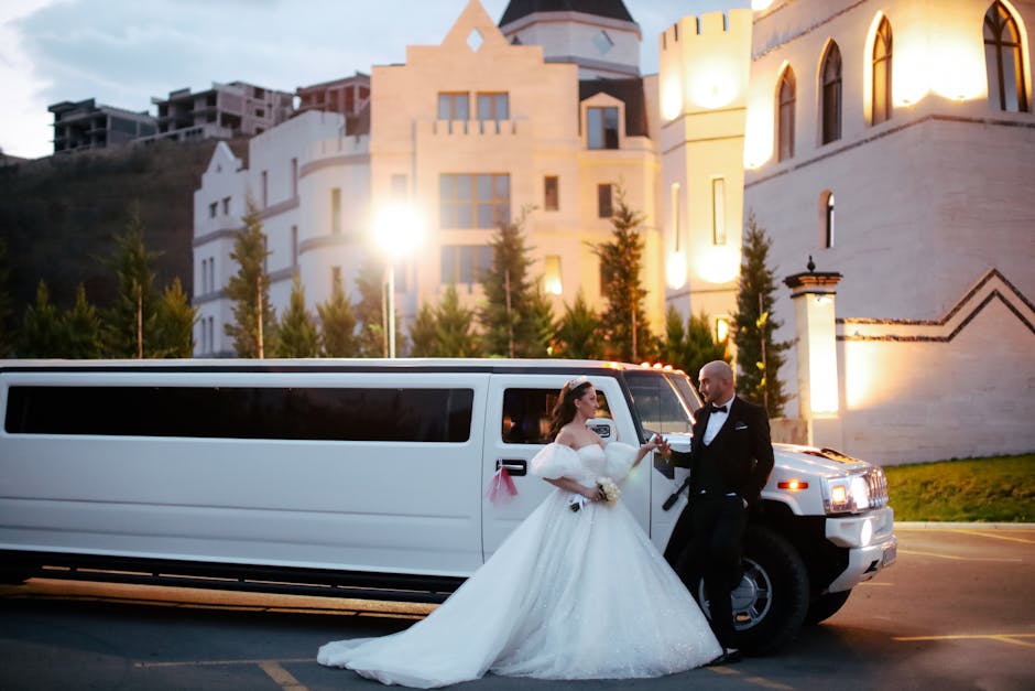 A bride and groom pose in front of a limo