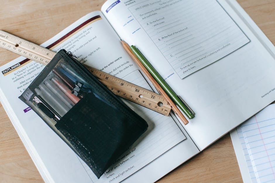 From above of textbook with exercises and ruler with pens near small case on table