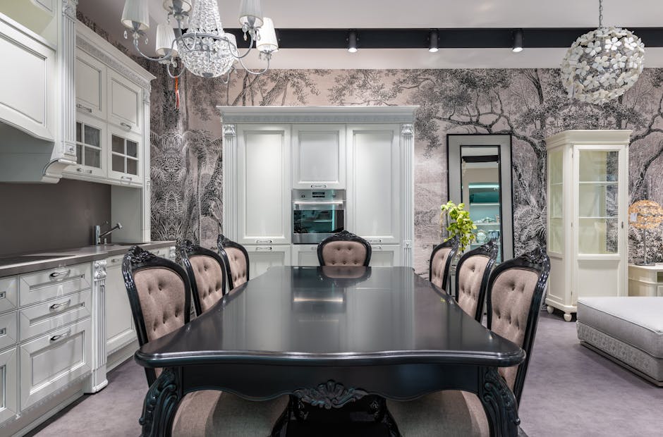 Black table with chairs placed near white cupboards and modern appliances in stylish spacious kitchen with mirror and creative wallpaper