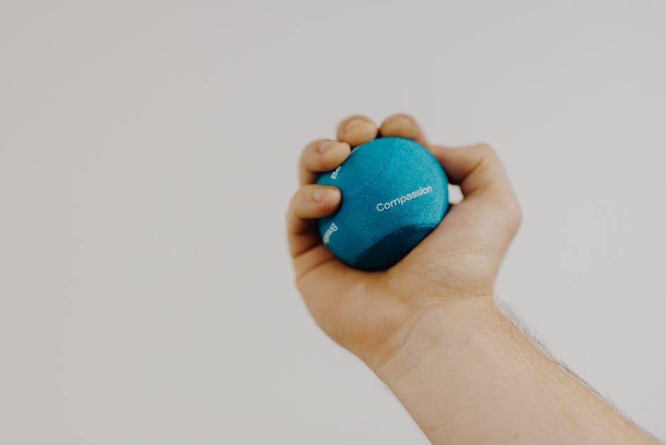 Crop unrecognizable male athlete with small rubber ball in hand exercising during recovery process on light background