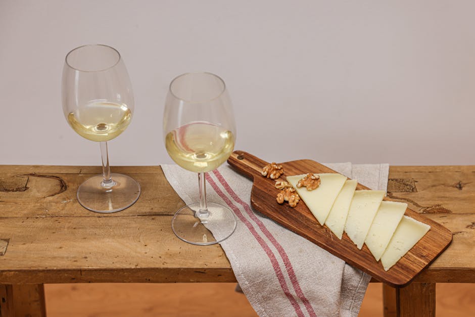 Glasses of Wine beside Walnuts and Slices of Cheese on a Wooden Chopping Board