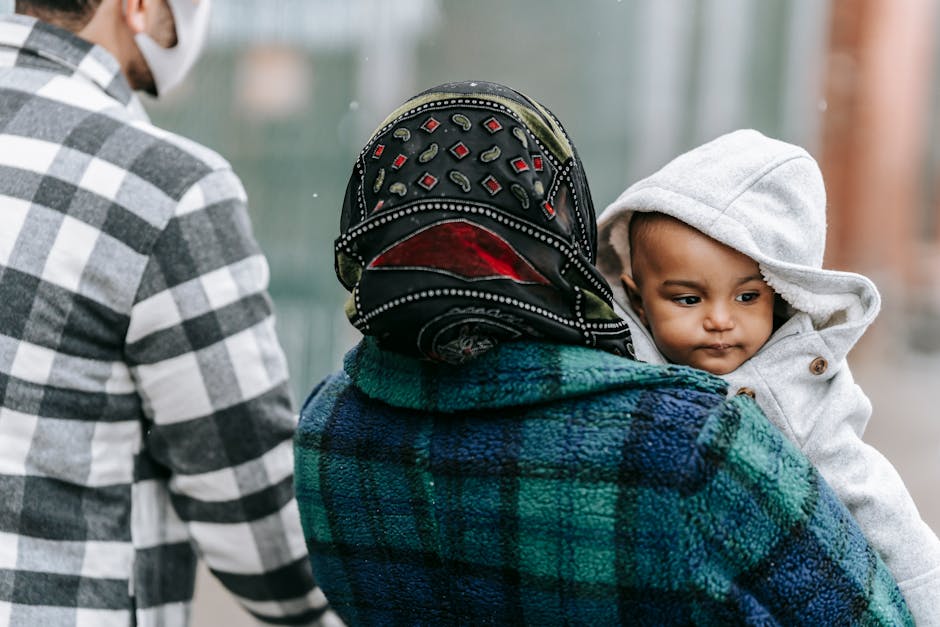 Anonymous father and mother with African American baby in warm outerwear on hands walking on street in city on blurred background