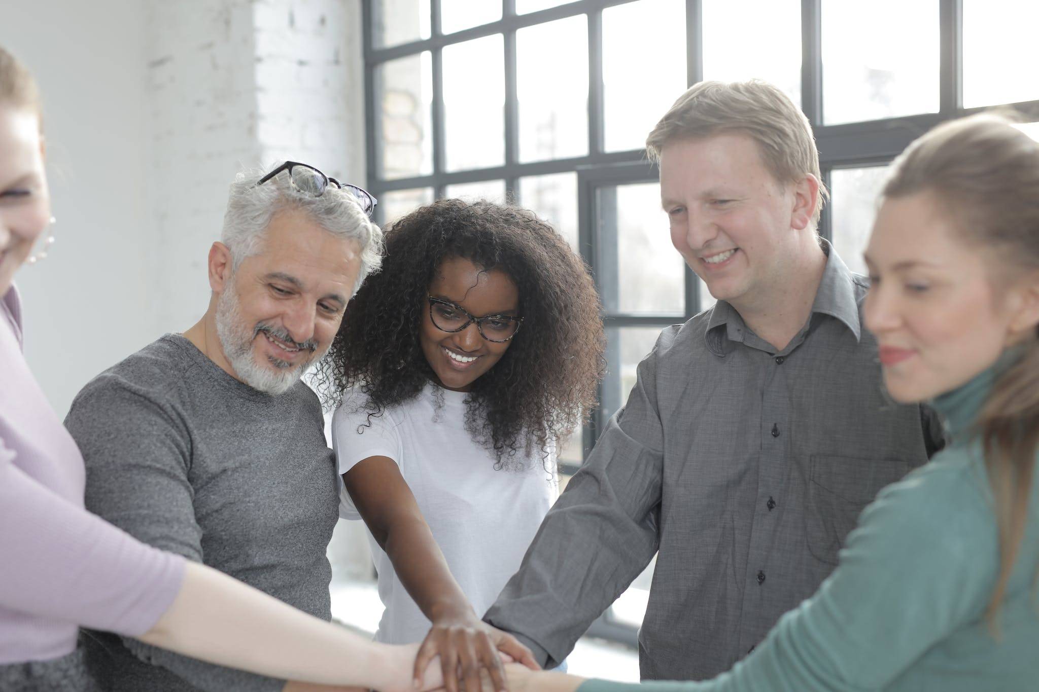 Happy diverse colleagues joining hands at work in afternoon