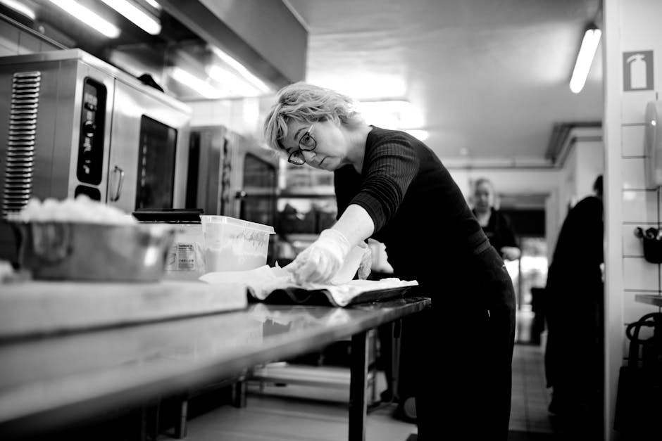 Black and white concentrated female chef standing at metal table in kitchen and preparing food in restaurant