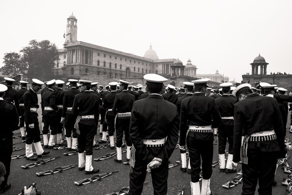 Black and white multiethnic men in military uniform standing in rows near automatic guns lying on ground during military parade on square near old buildings with turrets on daytime