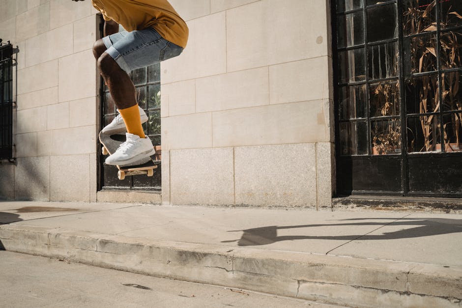 Side view of crop unrecognizable fit young black guy in stylish outfit doing trick on skateboard during workout on street on sunny day