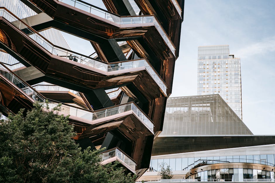 Low angle of futuristic geometric construction with stairs above bushes in city with skyscrapers in daylight