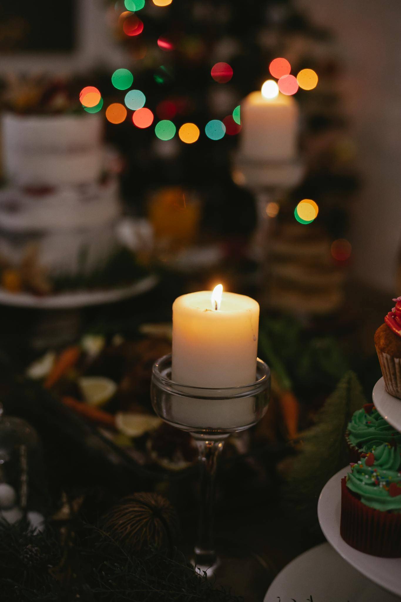 Festive dinner on table decorated with burning candle against fir tree with shining garland at Christmas Eve