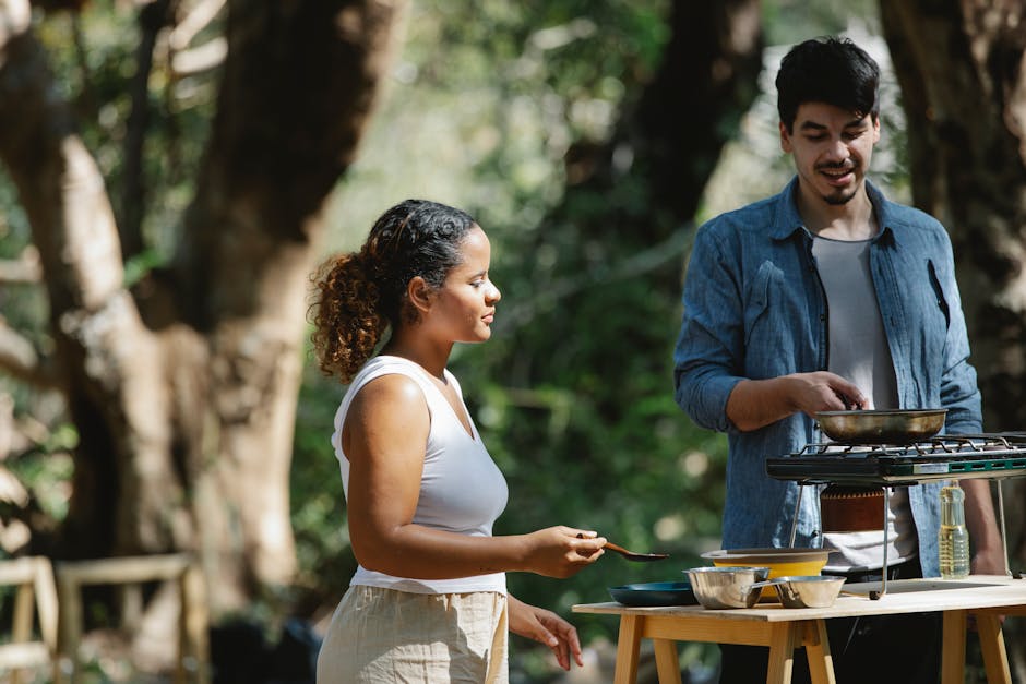 Focused multiethnic couple cooking on metal stove using skillet and spatula in woods