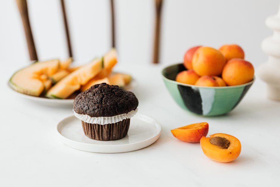 Halved ripe apricot near chocolate cupcake and assorted fruits on background