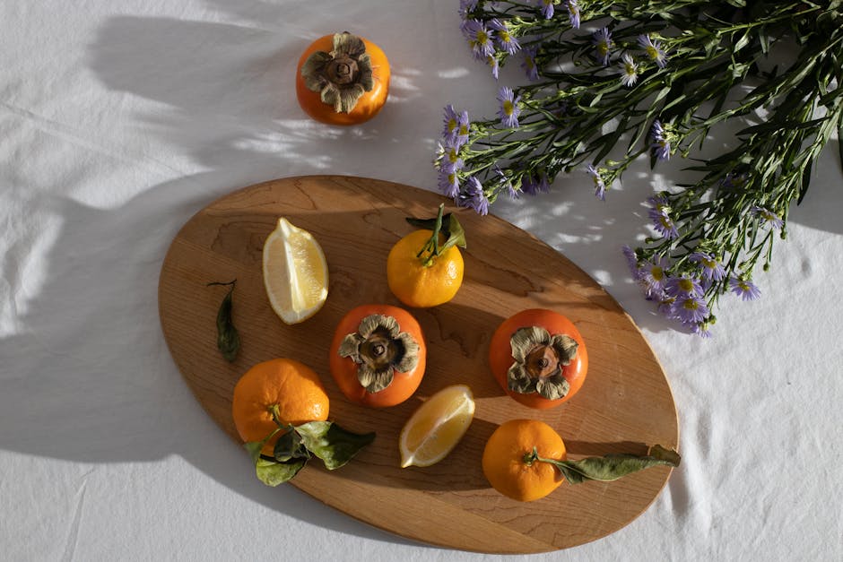 Top view of healthy ripe whole persimmons and tangerines placed on wooden cutting board with lemon slices near bunch of Aster amellus herbaceous flowers