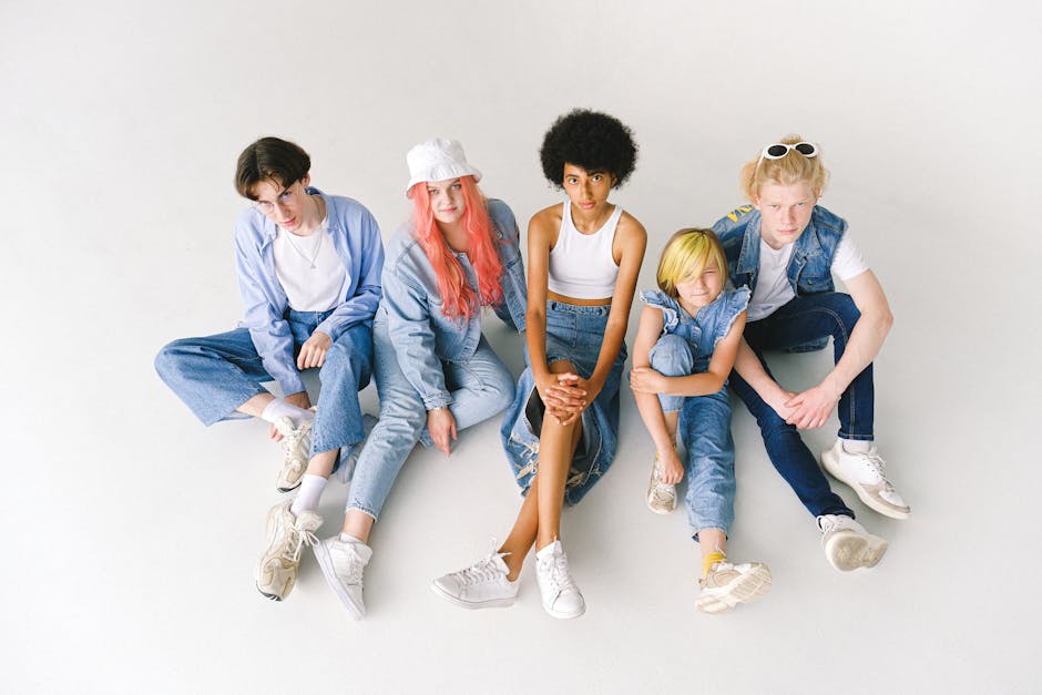 From above full body of diverse models wearing stylish denim outfits sitting on white floor in studio
