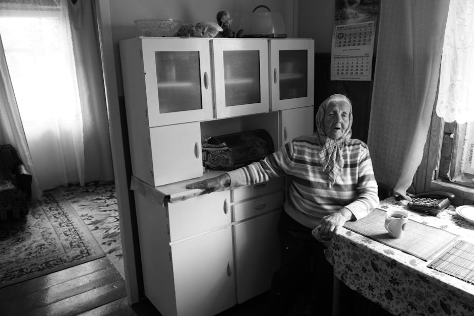 An old woman sitting at a table in her kitchen