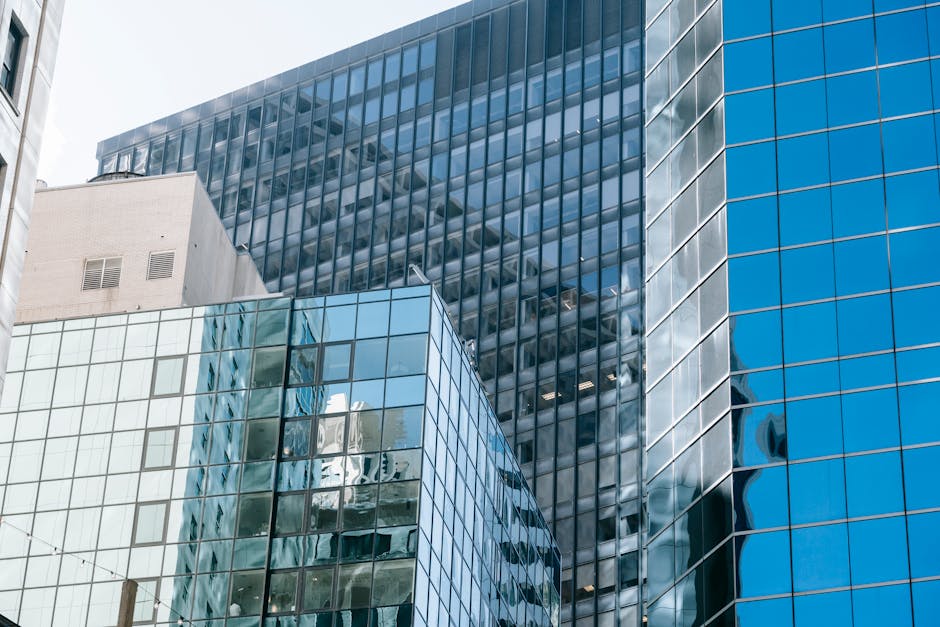 From below facade of modern multistory buildings with glass mirrored walls reflecting blue sky in city