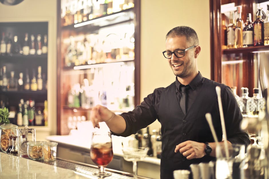 Happy young male barkeeper standing at counter and preparing alcohol cocktail for order while working in modern pub