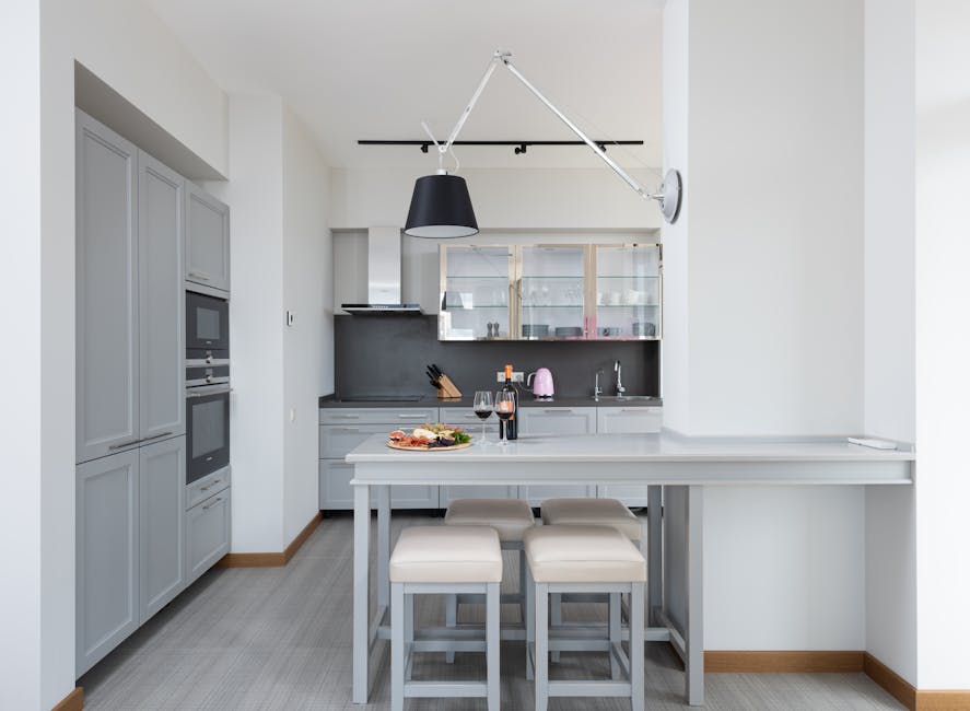 Bottle of red wine and glasses placed near plate with food on table in modern kitchen with light interior