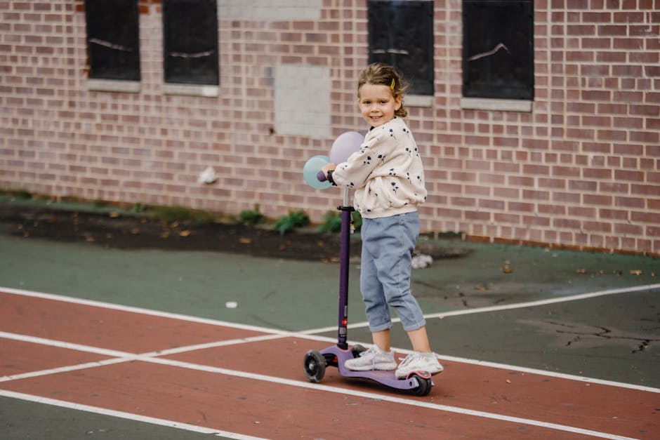 Content child in casual clothes with balloons riding electric scooter and looking at camera in town against building