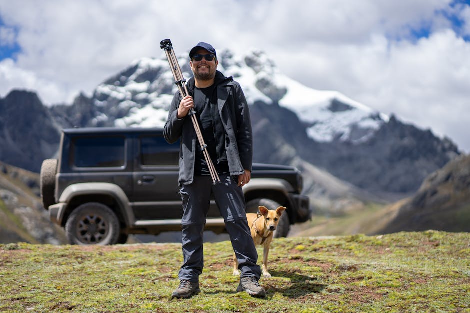 Smiling Man Standing with a Tripod and Dog in a Scenic Mountain Landscape