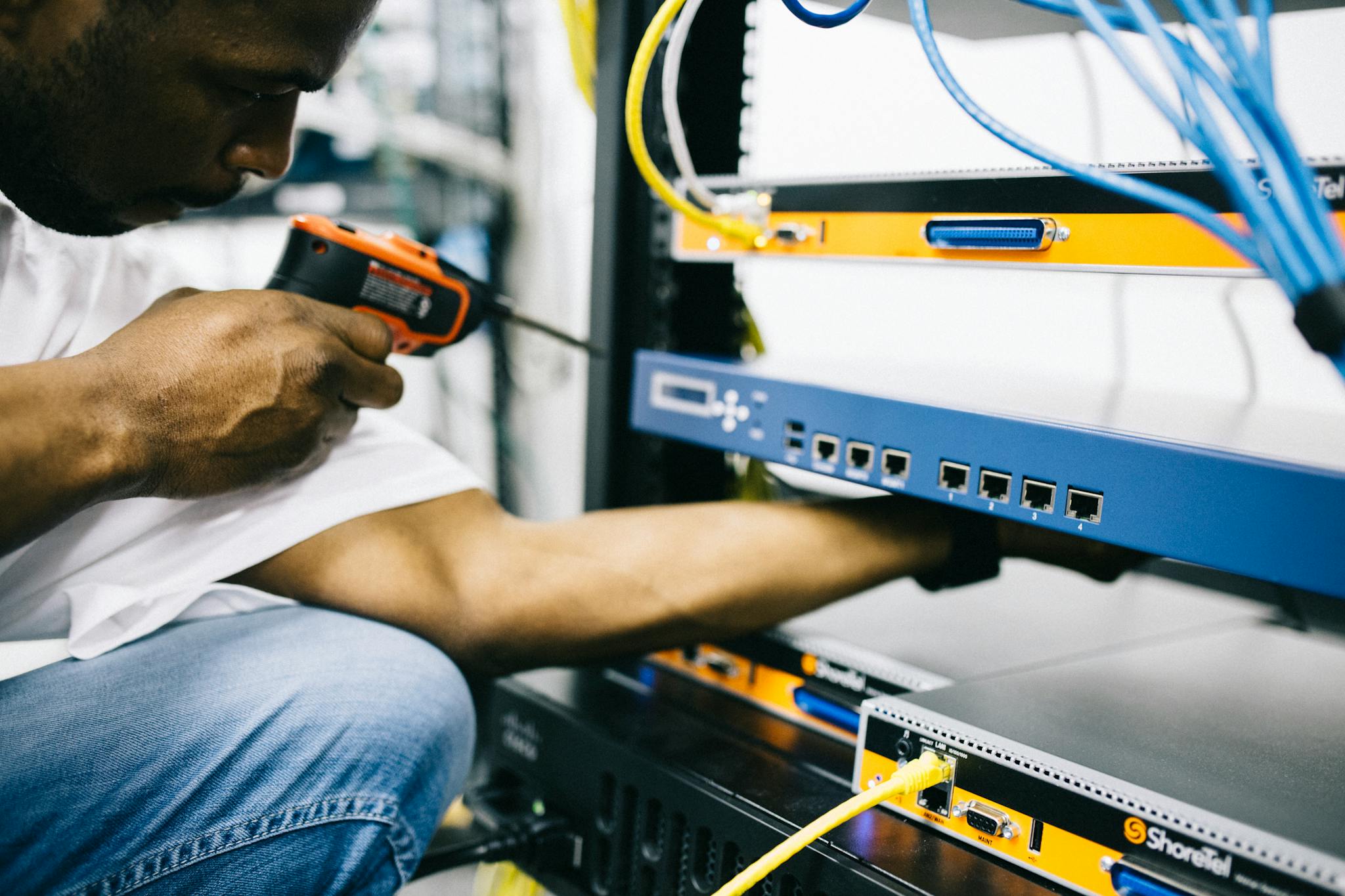 Side view crop concentrate African American male mechanic in jeans and white shirt using screw gun while working with hardware