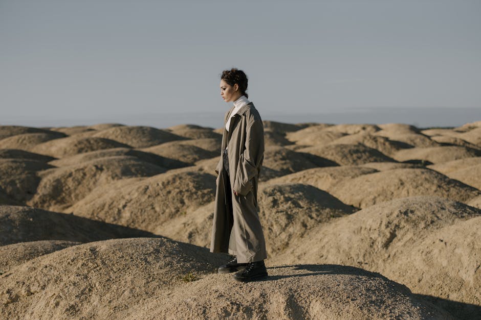 Man in Brown Coat Standing on Brown Sand