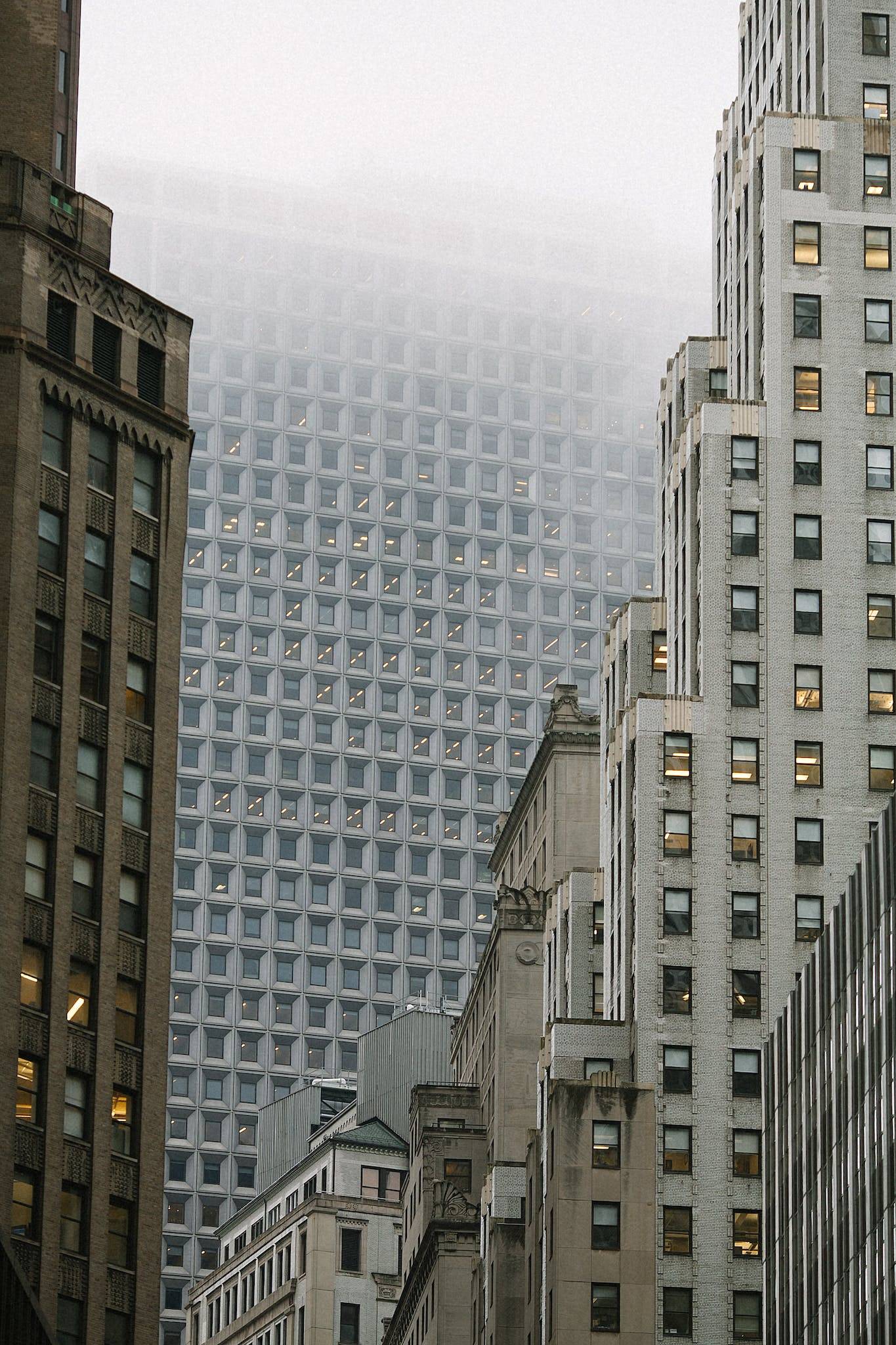 Low angle of modern multistage building exteriors with geometric windows on front walls in misty weather in town