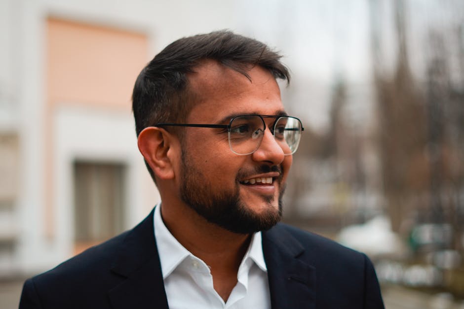 A man with glasses and a suit is smiling