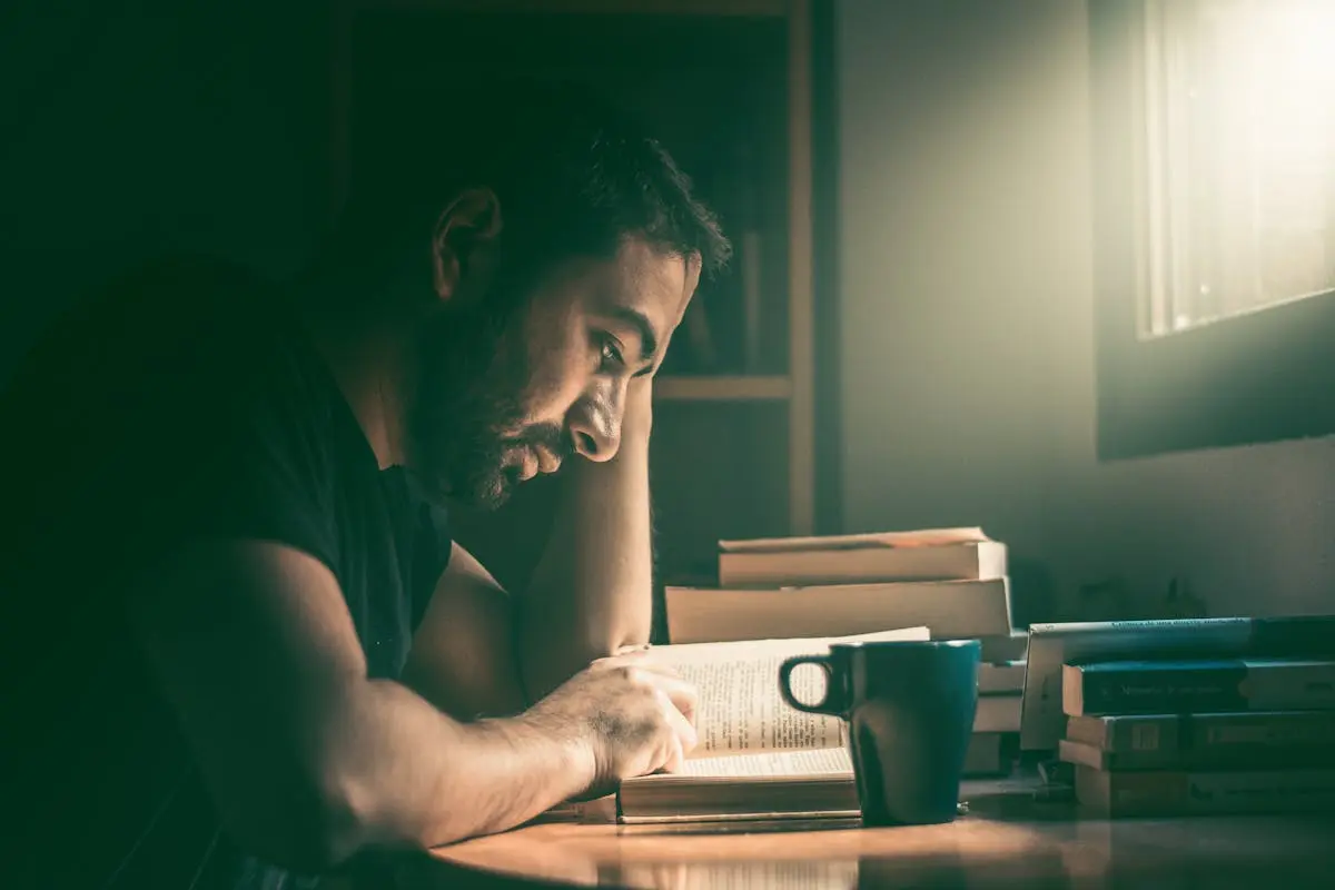 An adult man immersed in reading by the window in Madrid. Warm, focused study atmosphere.