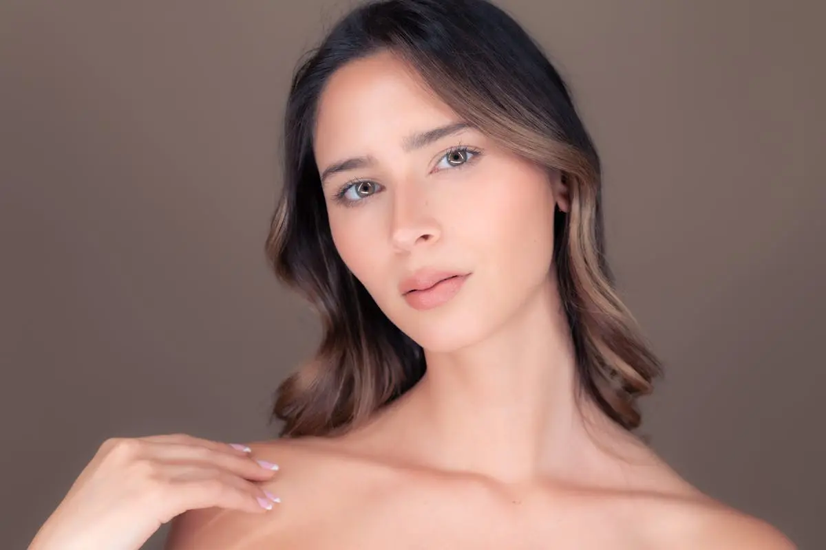 Close-up portrait of a young woman with brown hair against a soft brown background.