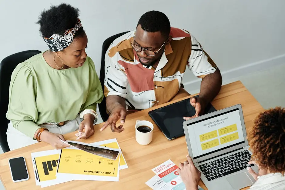 Three colleagues collaborate over marketing documents and a laptop in a modern office setting.