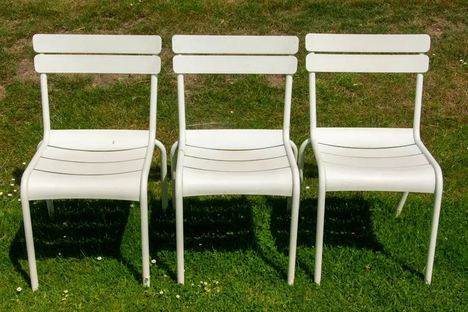 Three white garden chairs arranged on a fresh green lawn under daylight.