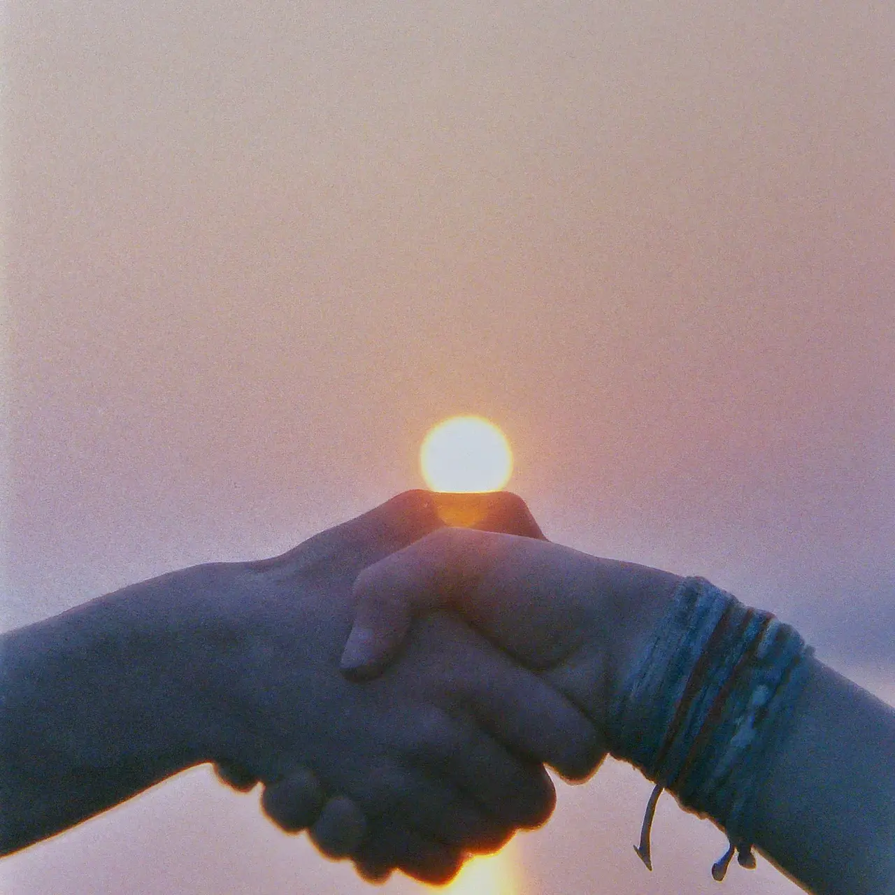 Two hands shaking in front of a sunrise. 35mm stock photo