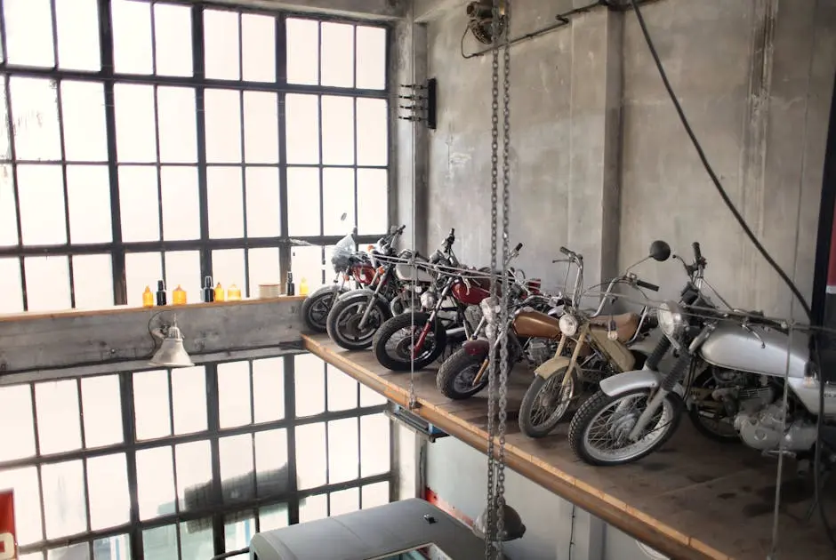 A collection of vintage motorcycles displayed on loft shelving in an industrial-style garage with large windows.