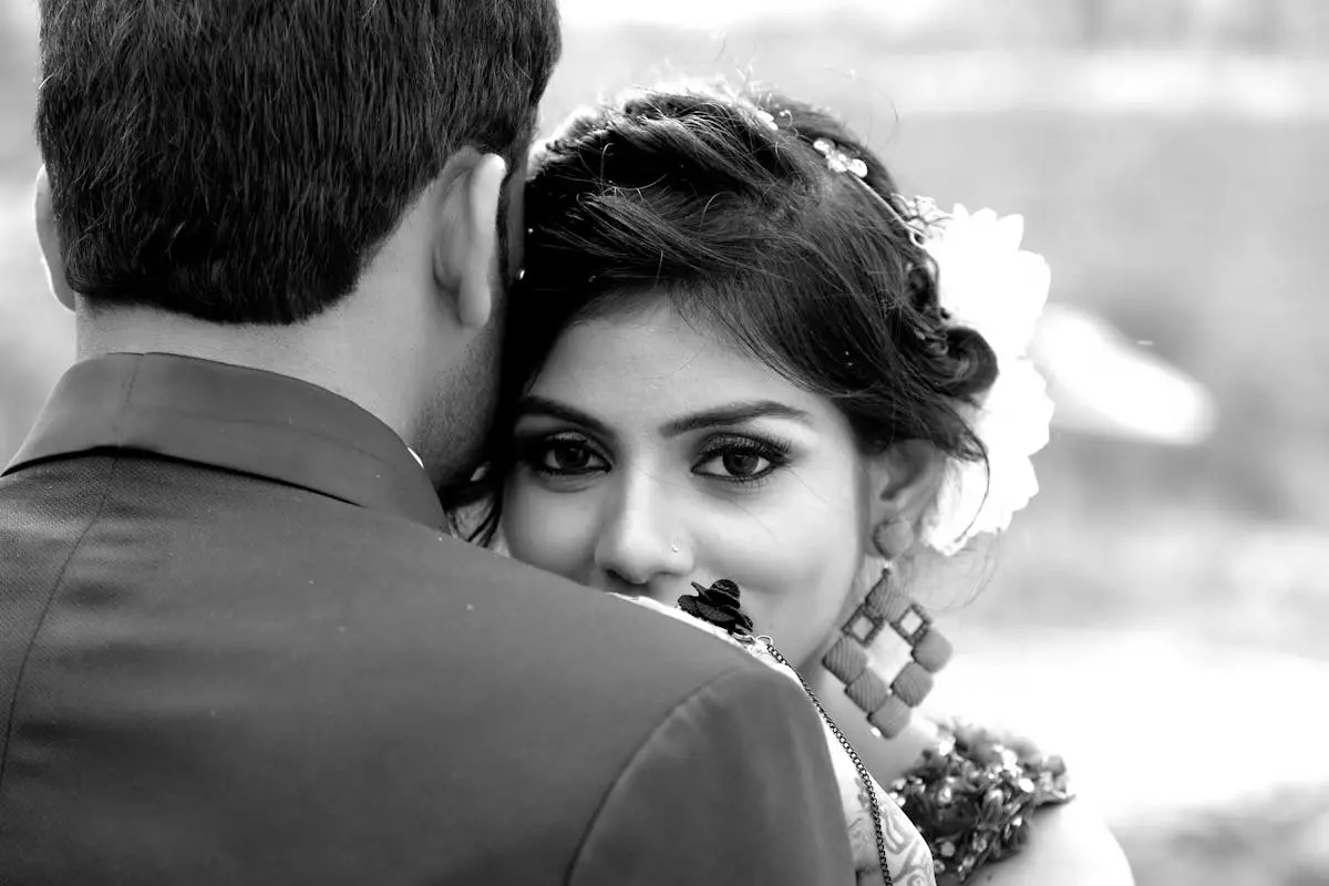 Close-up black and white portrait of a bride embracing her groom outdoors.