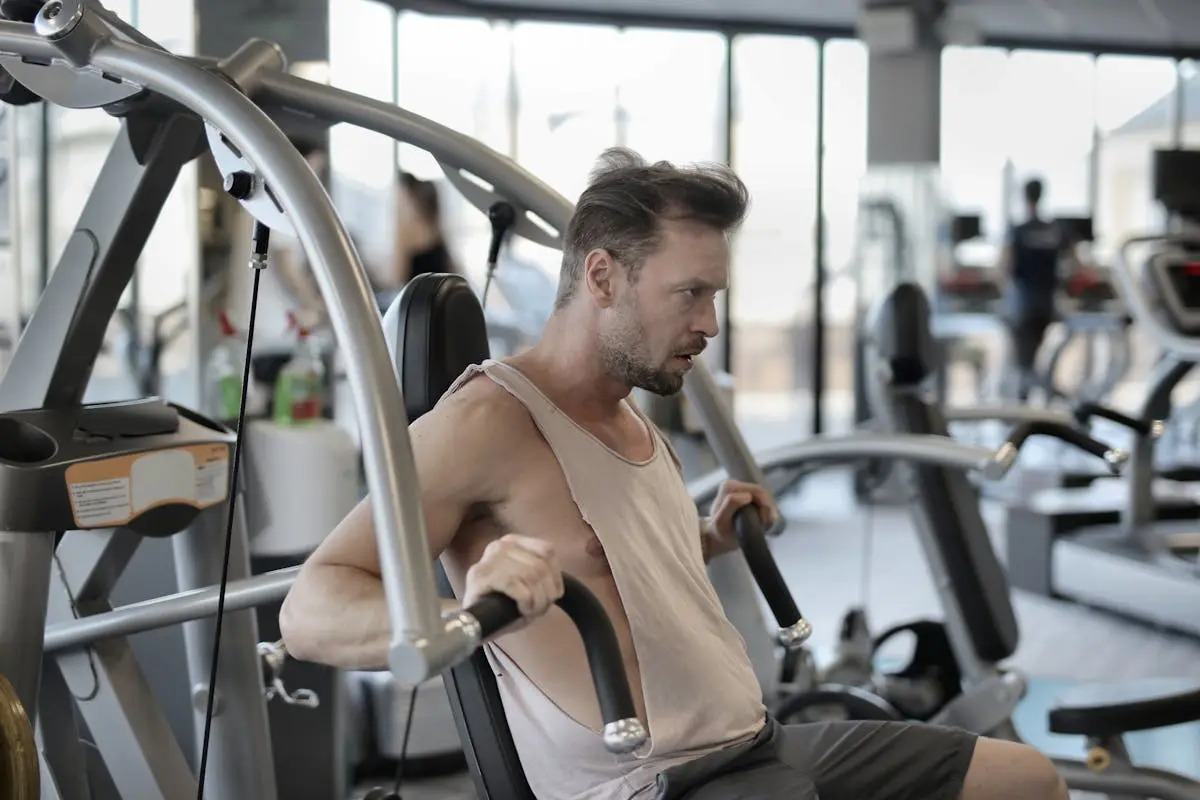 Strong sportsman exercising with shoulder press machine in gym