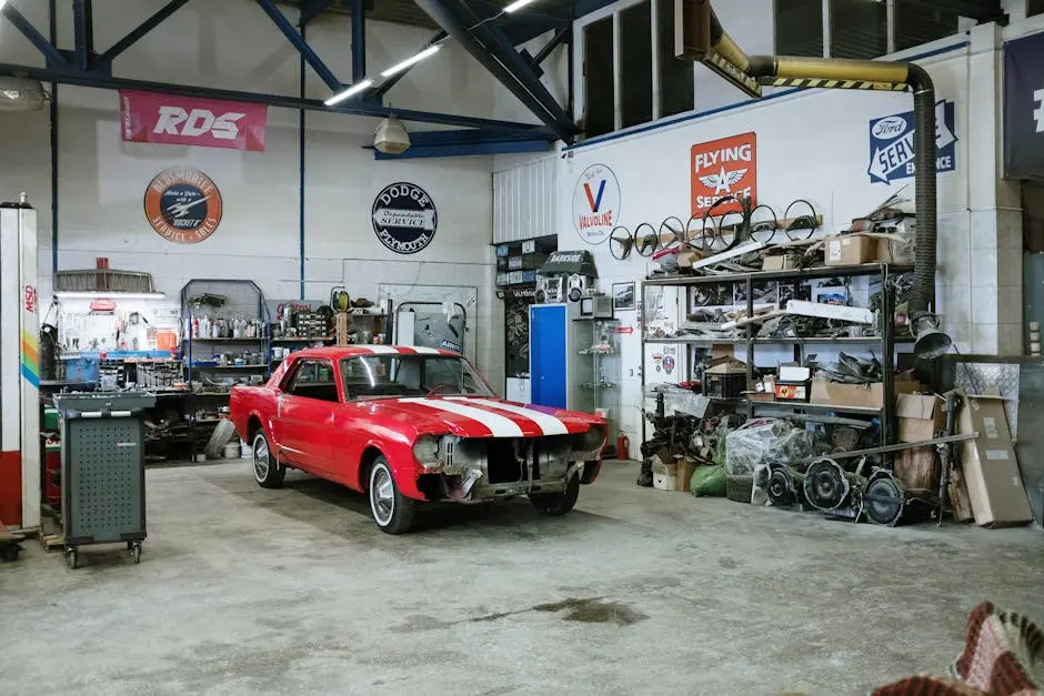 A vintage red car undergoing restoration in a well-equipped workshop with various tools and auto parts.