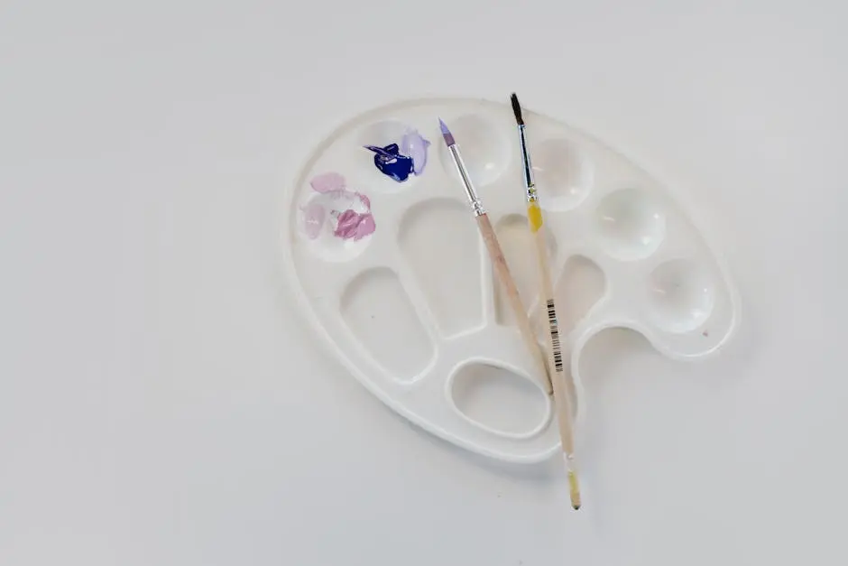 Flat lay of artist palette with brushes and paint on white surface, perfect for creative projects.