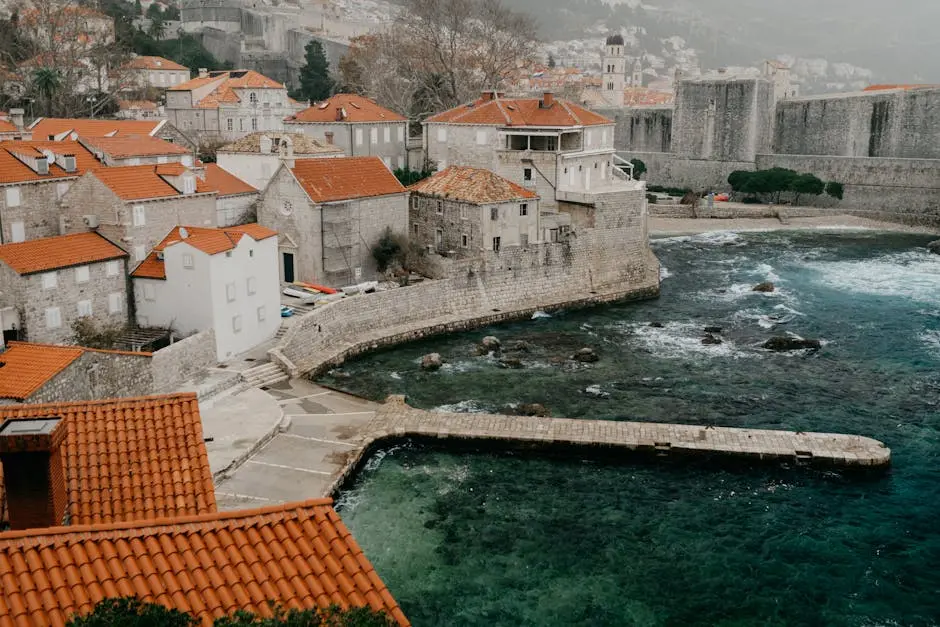 Historic stone buildings with red roofs along Dubrovnik’s coastline create a serene and picturesque scene.