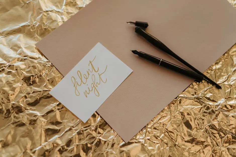 A stylish close-up of calligraphy pens and a Silent Night card on gold foil paper.