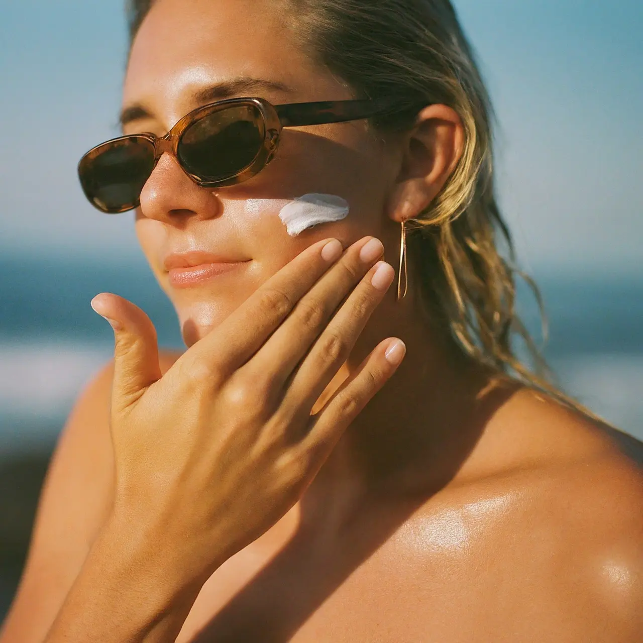 A person applying sunscreen lotion on their face at the beach. 35mm stock photo