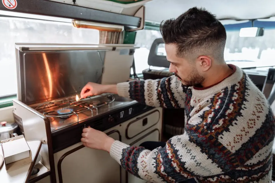 A man in a knitted sweater lighting a stove in a camper van kitchen, embodying cozy van life.