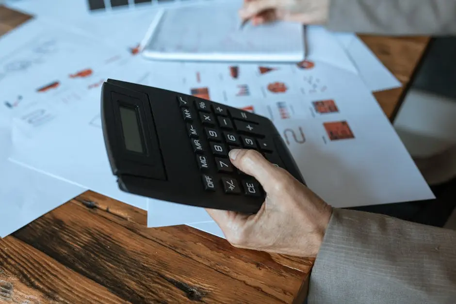 Close-up of a hand using a calculator on a wooden desk with charts.