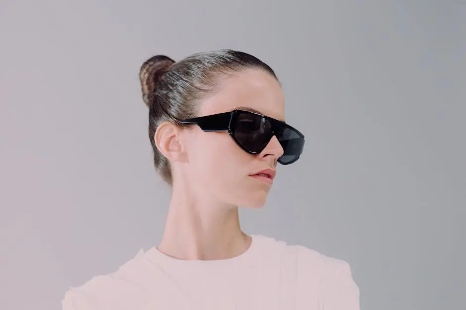 Stylish portrait of a woman wearing futuristic sunglasses, sleek hair, and a white outfit in a studio setting.