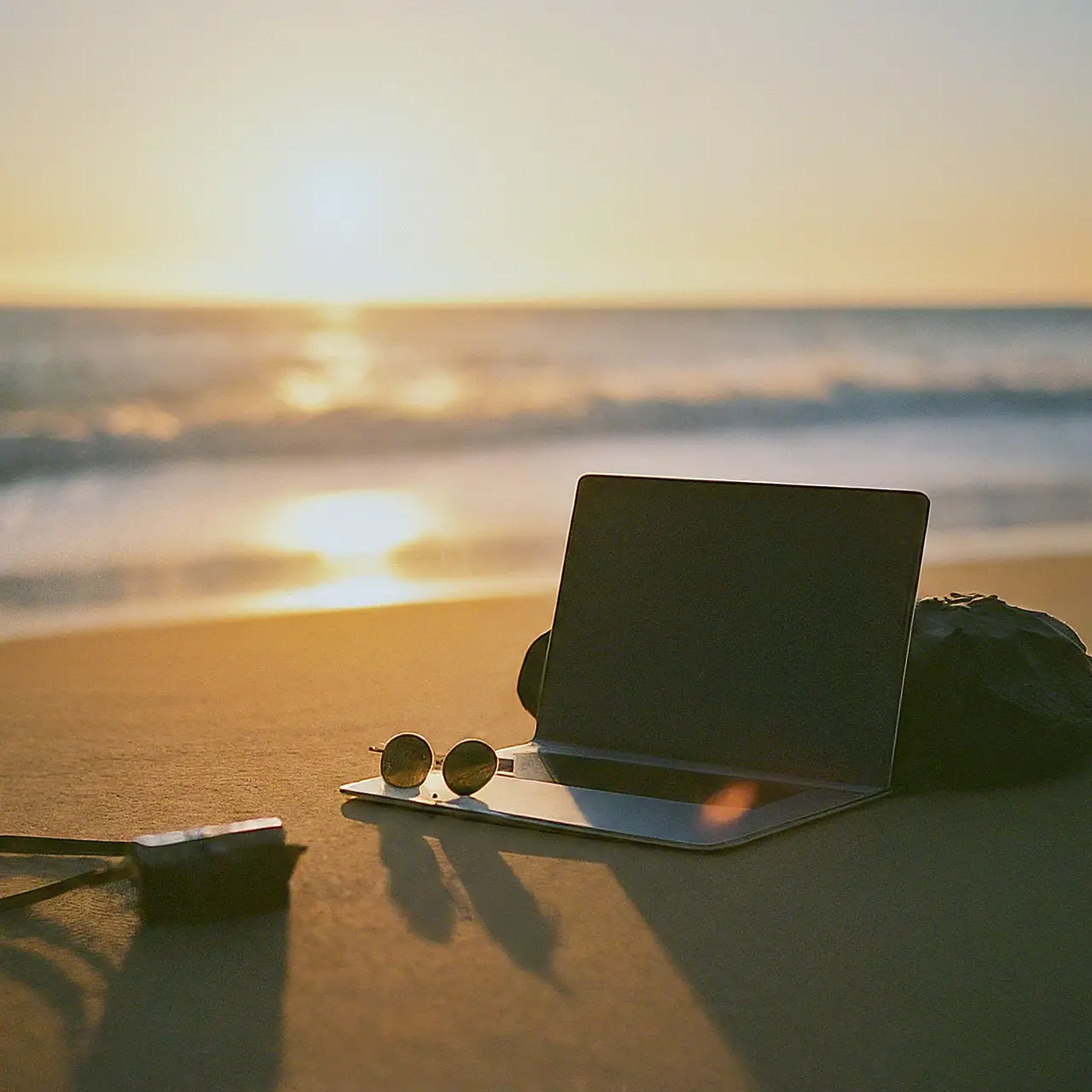 Laptop and travel gear on a beach at sunset. 35mm stock photo
